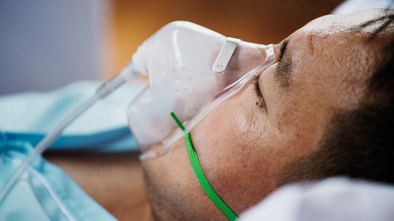 A man asleep on a hospital bed with an oxygen mask covering his nose and mouth.