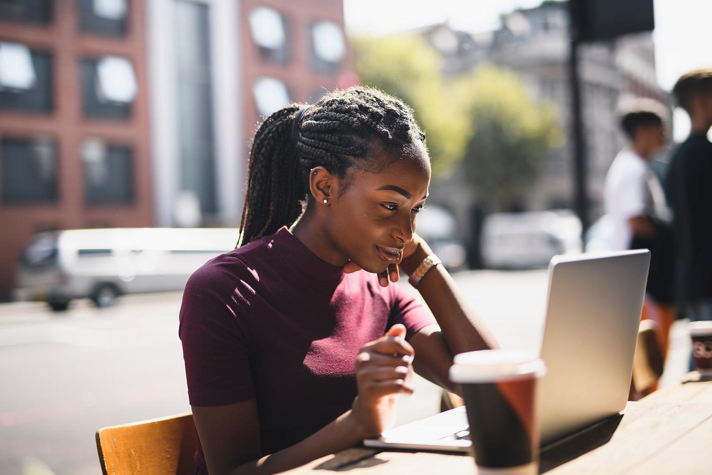 Woman with braids using a laptop at an outdoor cafe
