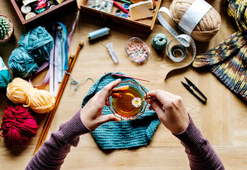 Aerial view of hands holding tea cup with knitting on wooden table 