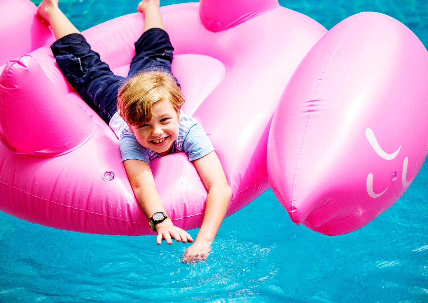 Aerial view of young caucasain boy floating in the pool with flamingo shape inflatable tube Aerial view of young caucasain boy floating in the pool with flamingo shape inflatable tube