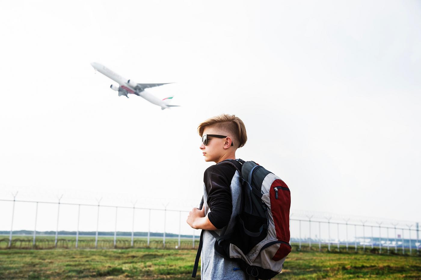 Young caucasian traveler standing outdoors with a takeoff airplane Young caucasian traveler standing outdoors with a takeoff airplane