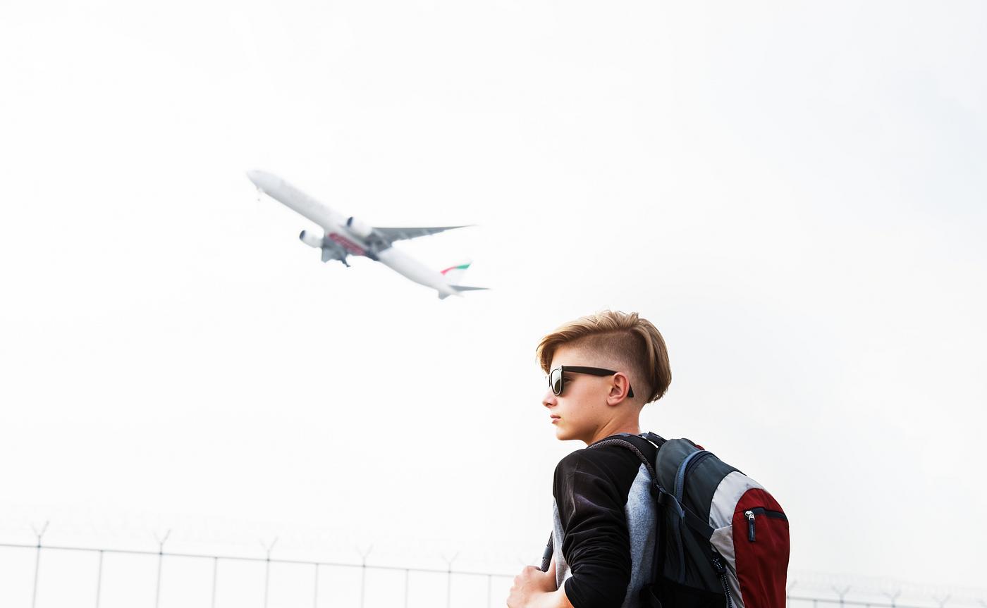 Young caucasian traveler standing outdoors with a takeoff airplane Young caucasian traveler standing outdoors with a takeoff airplane