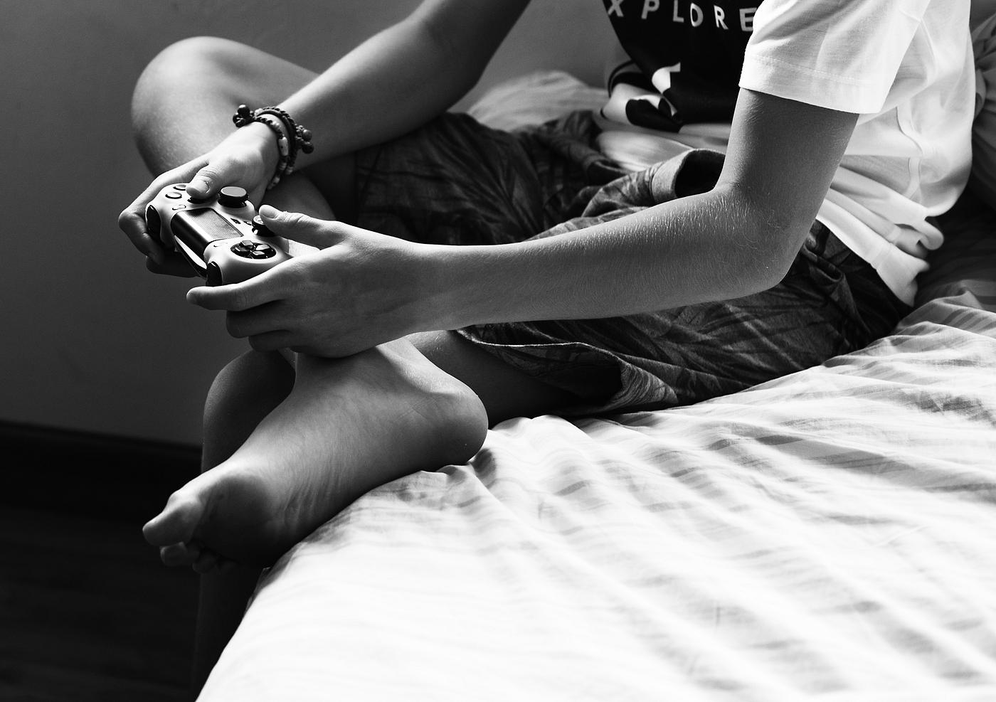 Young caucasian boy holding game control sitting on bed grayscale Young caucasian boy holding game control sitting on bed grayscale