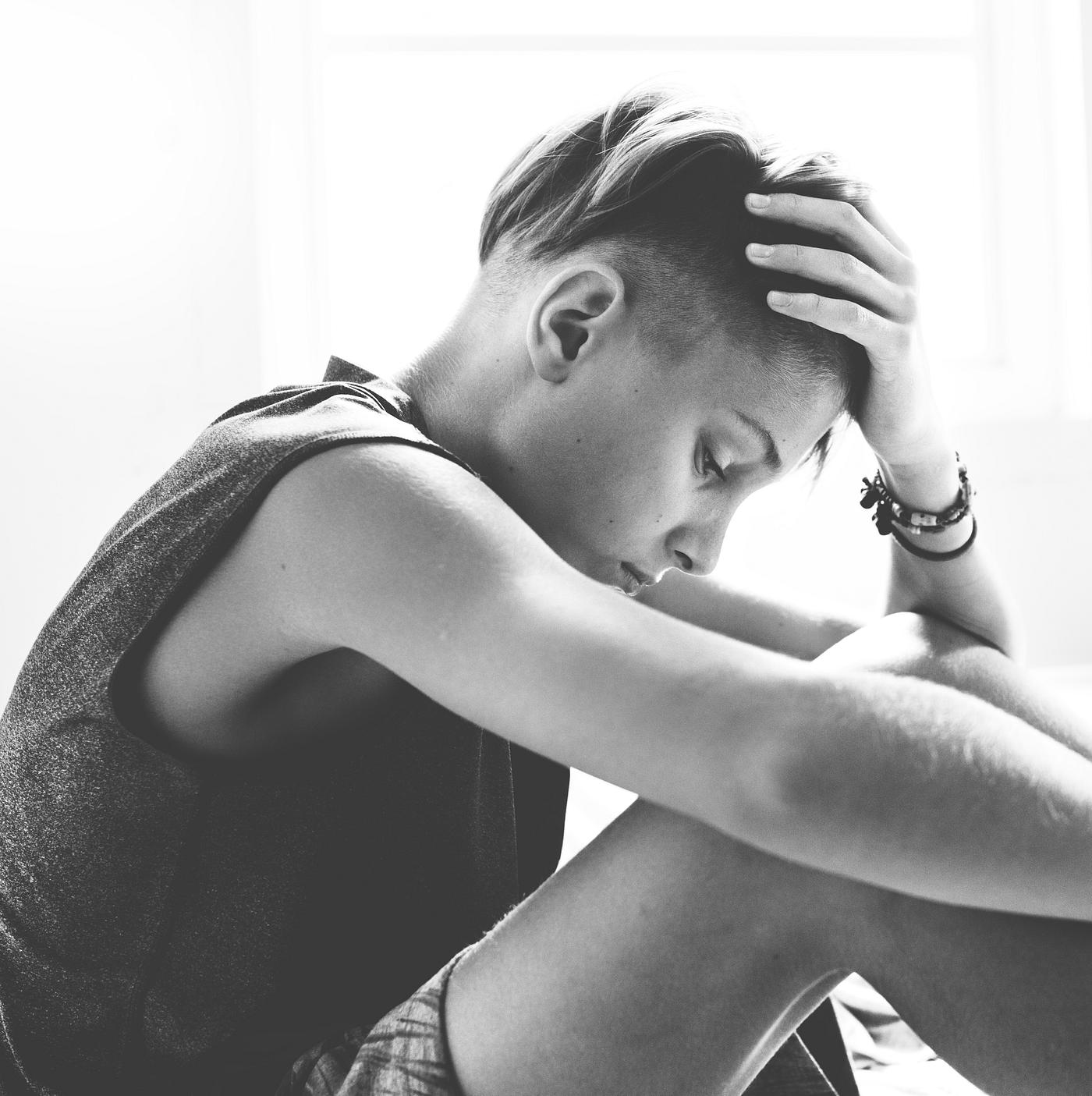 Closeup of young caucasian man sitting with face express of depressed upset emotion grayscale Closeup of young caucasian man sitting with face express of depressed upset emotion grayscale