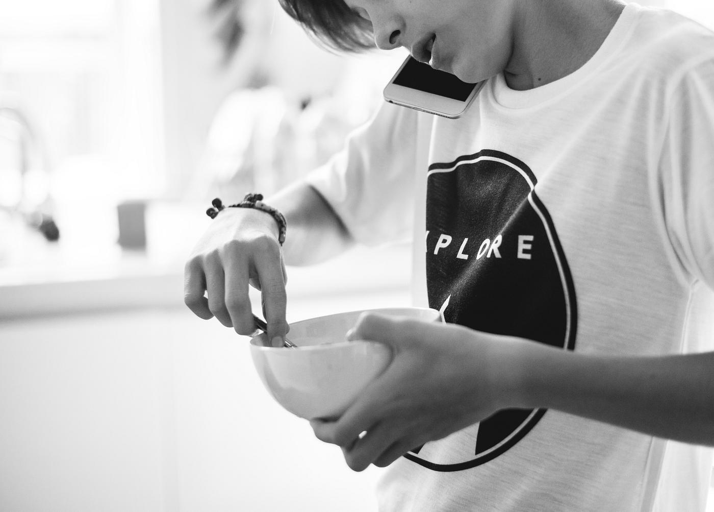 Closeup of young caucasain boy holding cereal bowl while talking on the phone in the kitchen grayscale Closeup of young caucasain boy holding cereal bowl while talking on the phone in the kitchen grayscale