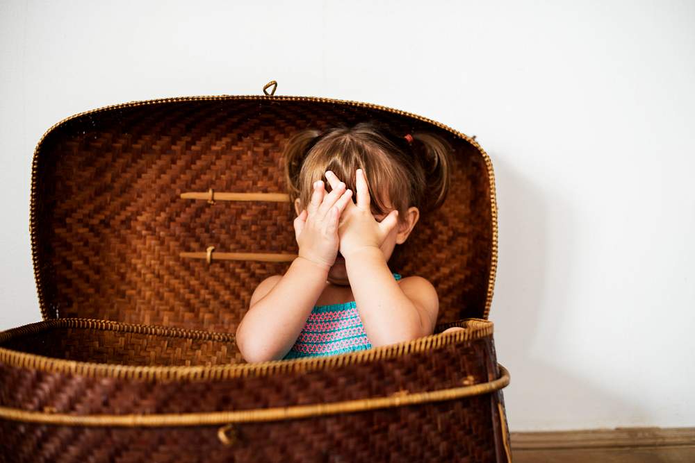 Little girl sitting in the basket and hands covering face 