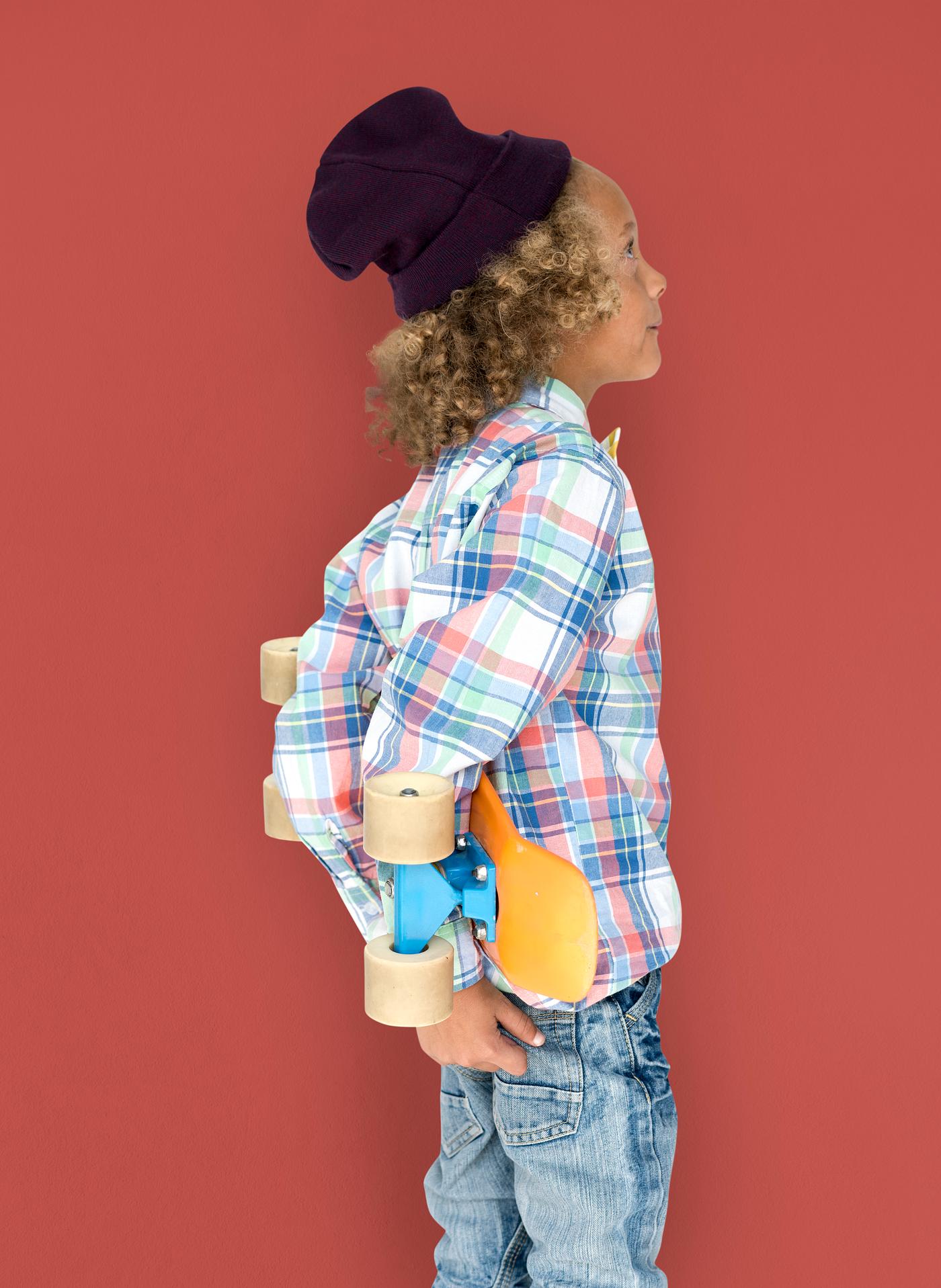 Boy holding a skateboard behind his back Boy holding a skateboard behind his back