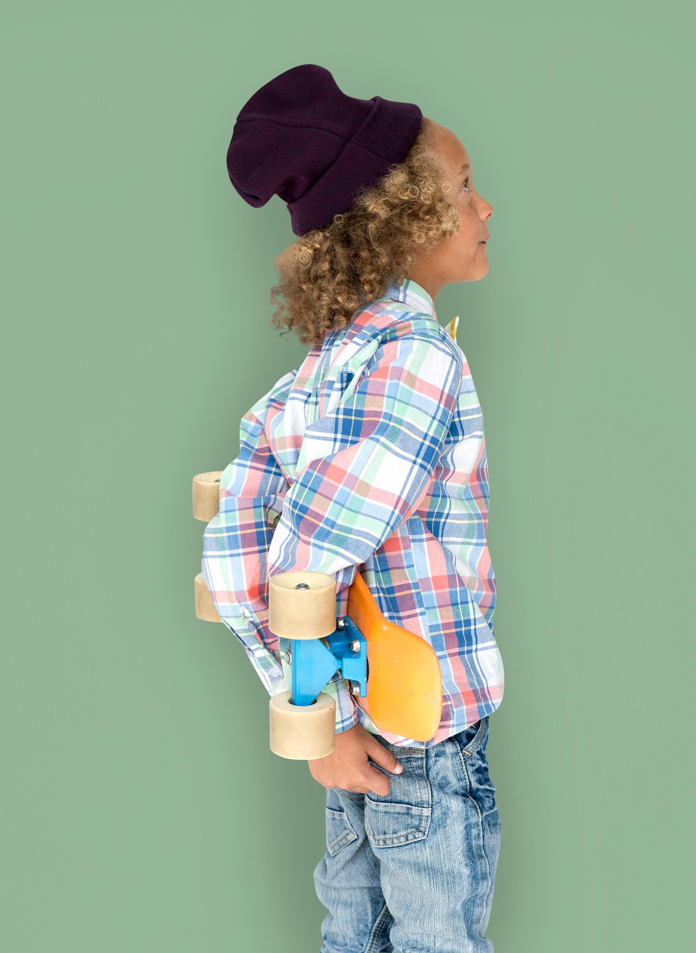 Boy holding a skateboard behind his back Boy holding a skateboard behind his back