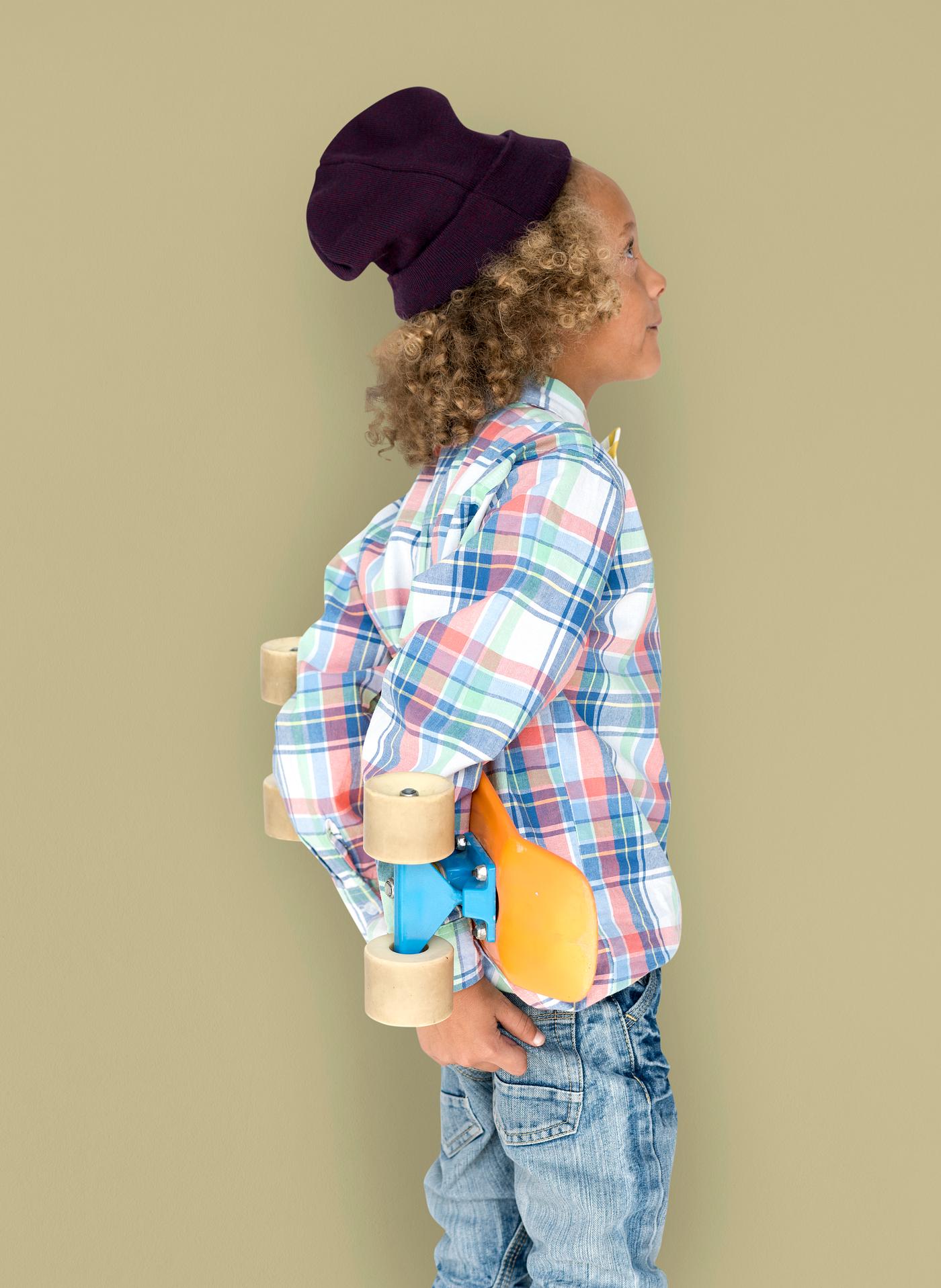 Boy holding a skateboard behind his back Boy holding a skateboard behind his back