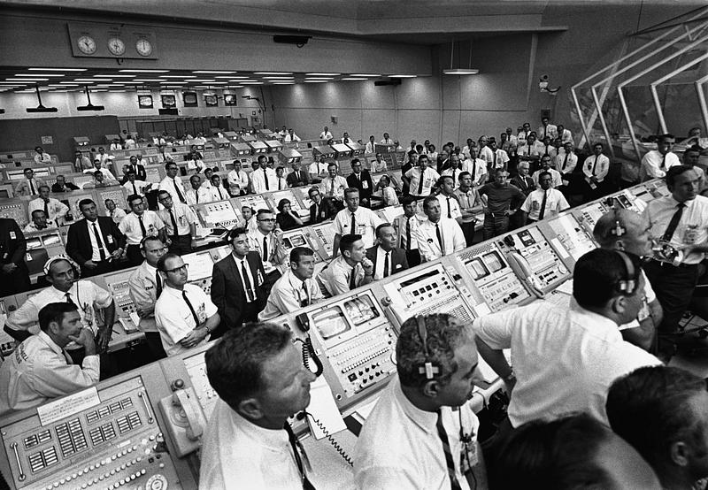 Moon landing photograph Members of the Kennedy Space Center government-industry team rise from their consoles within the Launch Control Center to…