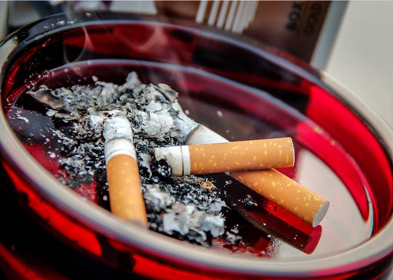 A ruby–colored glass ashtray contained three used cigarette butts along with their ashes. A healthcare provider donning…