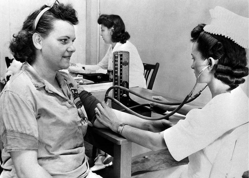 The 1950s historical photograph of a nurse taking her blood pressure of a woman ordnance worker in the hospital. Original…